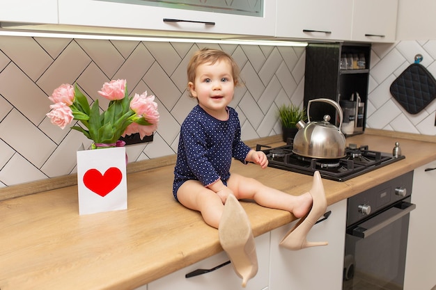 Ein süßes kleines Mädchen sitzt in der Küche mit einem Strauß rosa Tulpen, einer schönen Geschenkpostkarte