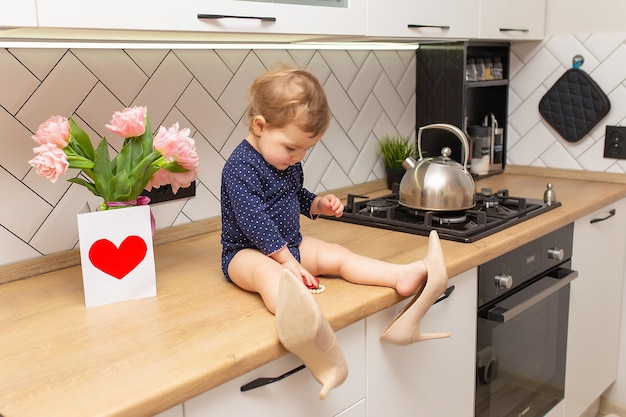 Ein süßes kleines Mädchen sitzt in der Küche mit einem Strauß rosa Tulpen, einer schönen Geschenkpostkarte