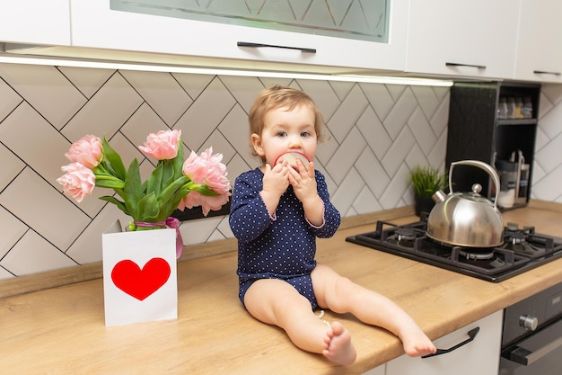 Ein süßes kleines Mädchen sitzt in der Küche mit einem Strauß rosa Tulpen, einer schönen Geschenkpostkarte