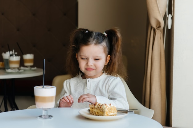 Ein süßes kleines Mädchen sitzt in einem Café und betrachtet eine Nahaufnahme von Kuchen und Kakao. Diät und richtige Ernährung.