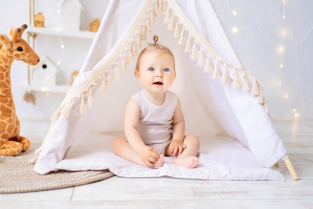 Ein süßes kleines Mädchen sitzt in einem hellen, gemütlichen Kinderspielzimmer Textilien für Kinder für das Kinderzimmer Ein glückliches Kind