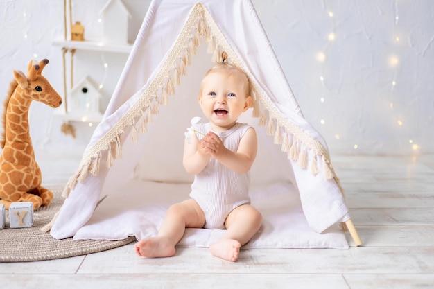 Ein süßes kleines Mädchen sitzt in einem hellen, gemütlichen Kinderspielzimmer Textilien für Kinder für das Kinderzimmer Ein glückliches Kind