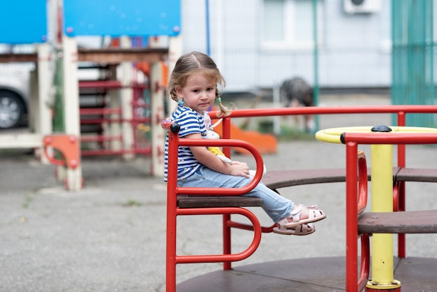 Ein süßes kleines Mädchen wirbelt allein auf einem roten Karussell auf einem verlassenen Spielplatz