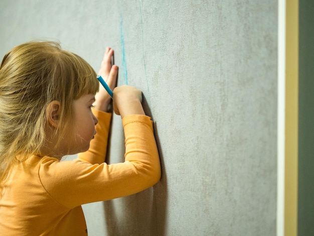 ein süßes kleines Mädchen zeichnet mit einem farbigen Bleistift an der Wand