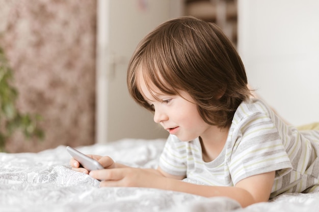 Ein süßes Kleinkind liegt im Schlafzimmer auf dem Bett und spielt mit dem Smartphone