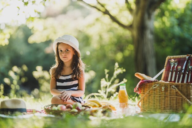 Ein süßes lächelndes kleines Mädchen sitzt auf einem Gras und genießt den Picknicktag im Park.