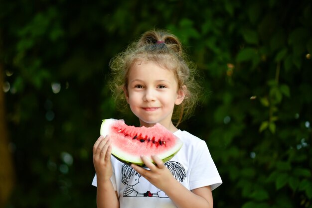 Ein süßes lächelndes Mädchen isst eine rote Wassermelone Hintergrund der grünen Blätter Nature Food Summer