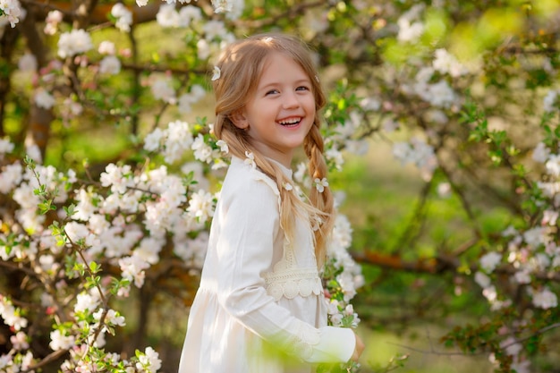 Ein süßes, lustiges kleines Mädchen in einem Kleid im Frühling in der Nähe eines blühenden Baumes lacht sanfte Fotografie