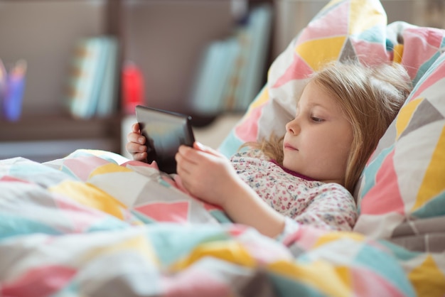 Ein süßes Mädchen benutzt das Telefon, während es auf dem Bett liegt