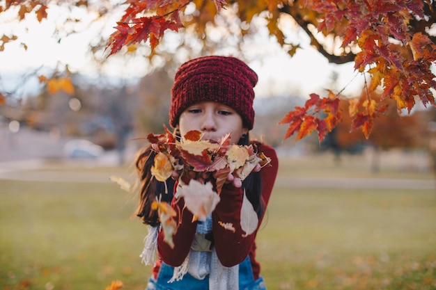Ein süßes Mädchen bläst ein Herbstblatt im Park