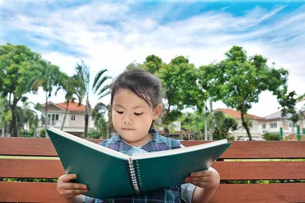 Ein süßes Mädchen liest ein Buch, während es auf einer Bank im Park sitzt