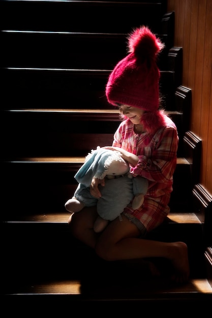 Foto ein süßes mädchen mit einem ausgestopften spielzeug sitzt zu hause auf der treppe