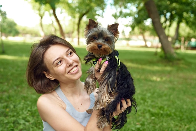 Ein süßes Mädchen mit einem Quadrat umarmt einen Yorkshire-Terrier auf der Straße Umarmungen mit Ihrem kleinen Hund