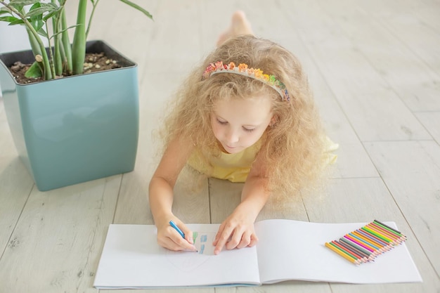 Ein süßes Mädchen mit lockigem Haar und blauen Augen zeichnet ein Album mit Buntstiften
