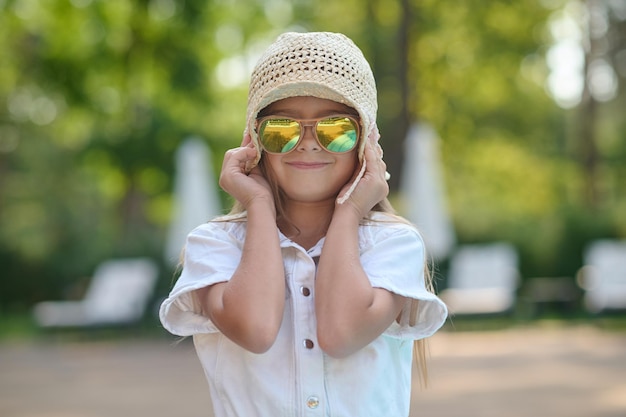 Ein süßes Mädchen mit Sonnenbrille und Whote-Hut, das glücklich aussieht