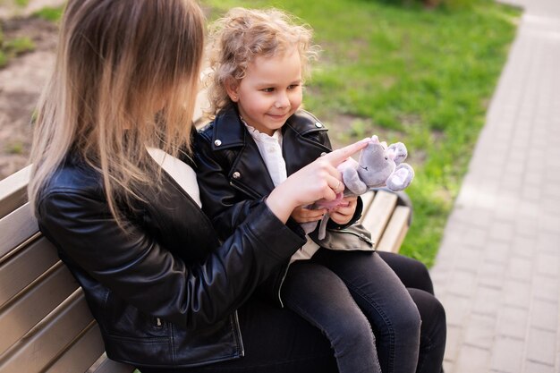 Ein süßes Mädchen mit weißen Locken sitzt auf dem Schoß ihrer Mutter und betrachtet ein Spielzeug