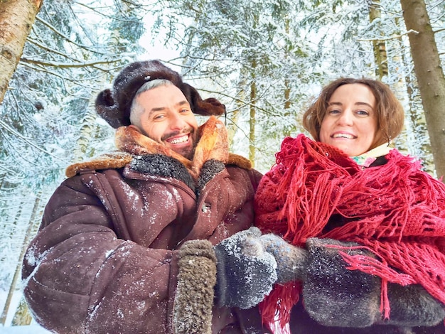 Ein süßes Paar mittleren Alters umarmt sich in einem schneebedeckten Wald im Winter bei einem Fotoshoot in stilisierten Kleidungsstücken der