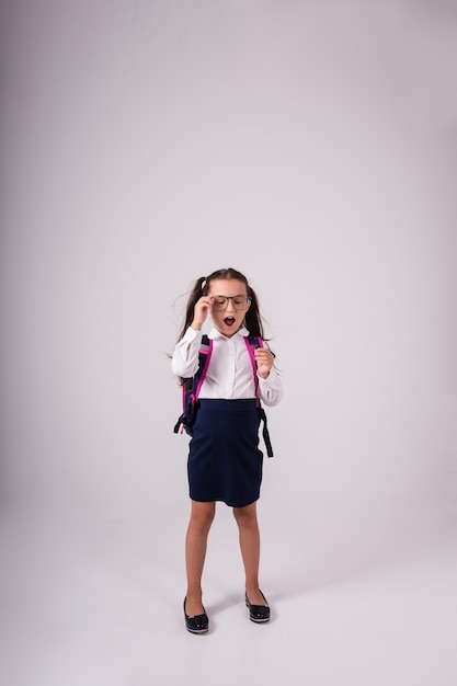 Ein süßes Schulmädchen in Uniform mit Brille steht auf weißem Hintergrund mit Platz für Text