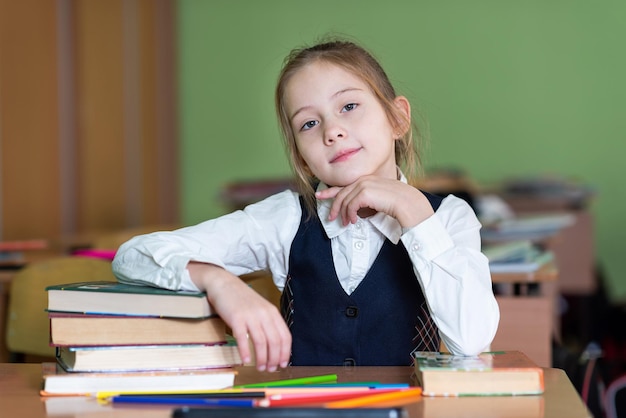 Ein süßes Schulmädchen sitzt an einem Schreibtisch, umgeben von Büchern Schaut in die Kamera Schulleben