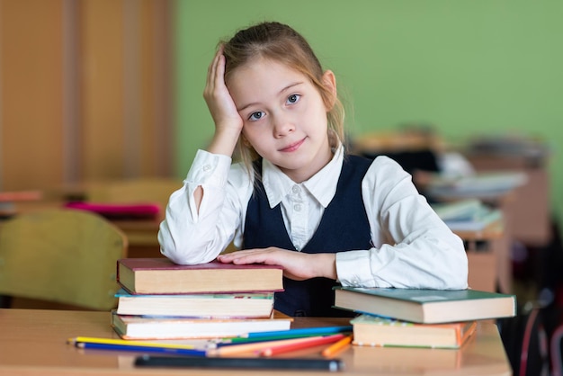 Ein süßes Schulmädchen sitzt an einem Schreibtisch, umgeben von Büchern Schaut in die Kamera Schulleben