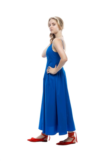 Ein süßes Teenager-Mädchen in einem blauen femininen Kleid und roten Schuhen, die auf weißem Hintergrund vertikal isoliert sind