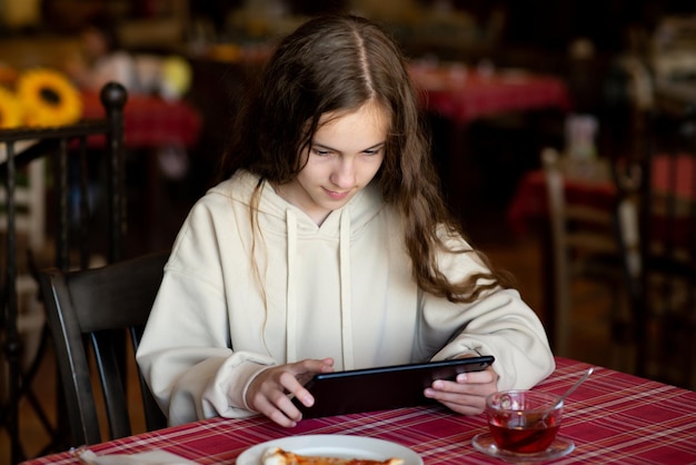 Ein süßes Teenager-Mädchen sitzt mit einem Gadget in der Hand in einem Café. Verwenden Sie Gadgets der Generation Z