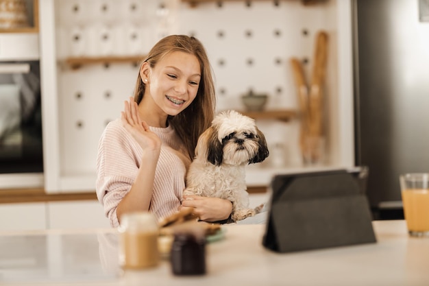 Ein süßes Teenager-Mädchen sitzt mit ihrem süßen Hund und macht einen Videoanruf auf einem digitalen Tablet bei ihr zu Hause.