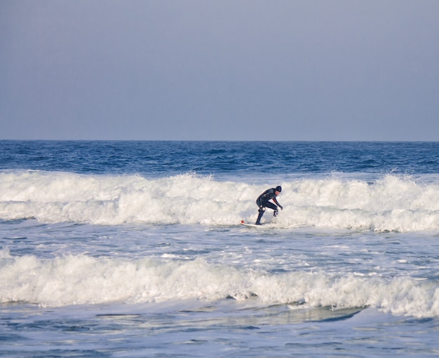 Ein Surfer reitet in einem Neoprenanzug Wellen im Wasser. Wellenspritzen. wasserdichter Anzug