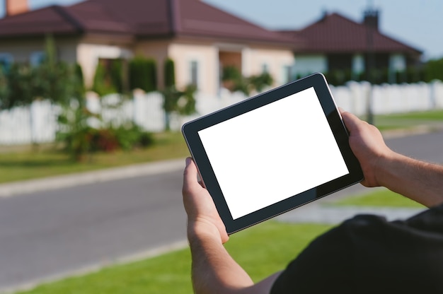 Ein Tablet in den Händen eines Mannes vor dem Hintergrund eines Hauses.