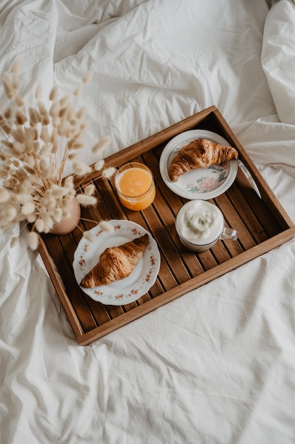 Ein Tablett mit Frühstücksartikeln auf einem Bett mit einer Tasse Orangensaft und einem Croissant