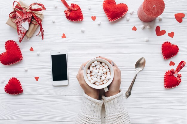 Ein Tasse Kaffee, dekorative Herzen, Geschenke und Smartphone auf einer weißen Tabelle für den Valentinstag