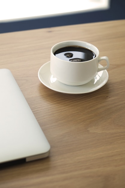 ein Tasse Kaffee mit Laptop auf Schreibtischhintergrund in der Vertikale