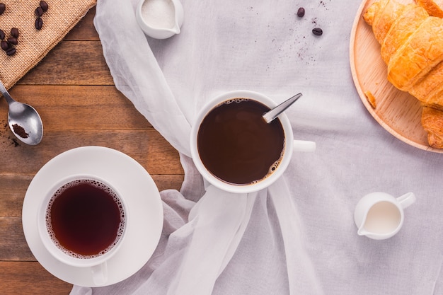 Foto ein tasse kaffee mit milch-, zucker- und hörnchenbrot auf holztisch, draufsicht