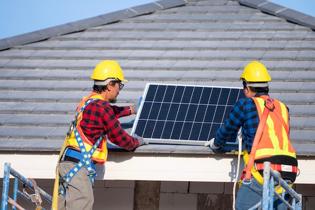 Ein Team asiatischer Techniker installiert Sonnenkollektoren auf dem Dach eines Hauses Querschnittsansicht des Bauherrn im Helm, der das Konzept des Solarmodulsystems für erneuerbare Energien installiert