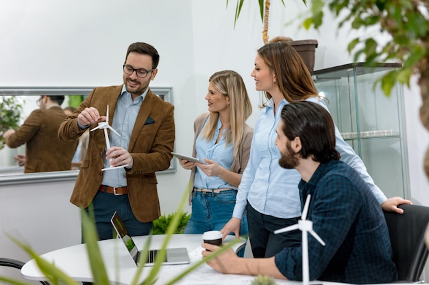 Ein Team intelligenter, qualifizierter junger Ingenieure, die über das Projekt alternativer Energien diskutieren, und einer von ihnen hält das winzige Modell einer Windmühlenturbine in der Hand und erklärt, wie es funktioniert.