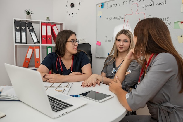 Ein Team von weiblichen Ärzten und Krankenschwestern benutzt gemeinsam einen Laptop, während sie am Schreibtisch im Besprechungsraum sitzen