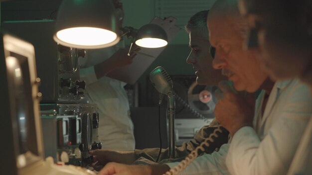 Ein Team von Wissenschaftlern arbeitet in einem Kontrollraum im Vintage-Stil. Sie benutzen Computer und telefonieren
