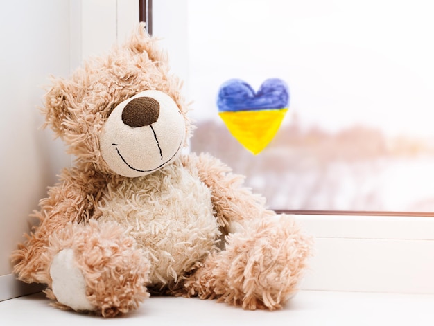 Ein Teddybär auf der Fensterbank und ein gemaltes Herz mit der ukrainischen Flagge