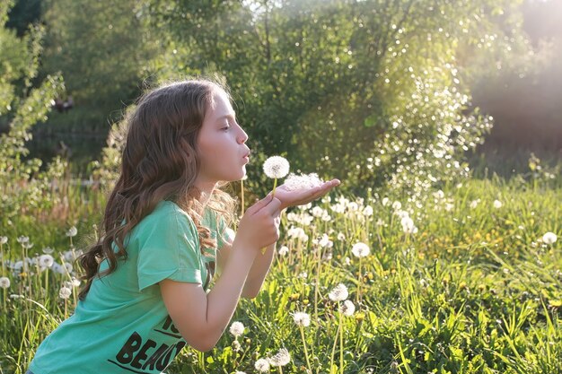 Ein Teenager bläst Samen von einer Löwenzahnblume in einem Frühlingspark