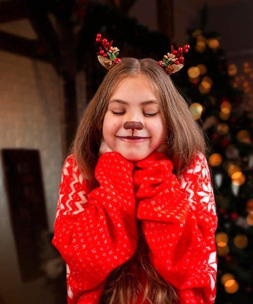 ein Teenager, das als Weihnachtsrentier gegen den Hintergrund eines Weihnachtenbaums gekleidet ist