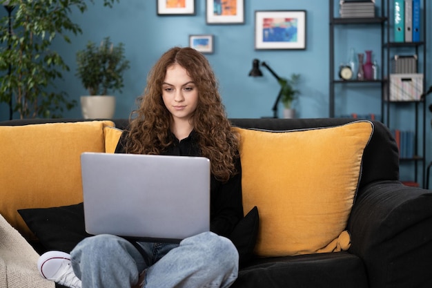 Ein Teenager entspannt sich auf einer Couch im Wohnzimmer zu Hause, das Mädchen benutzt die Laptop-Browsing-Website