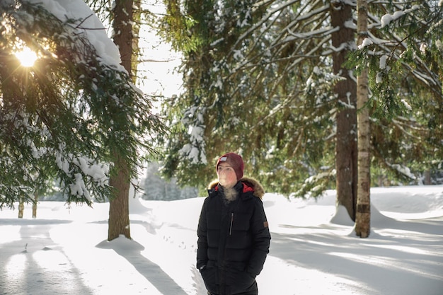 Ein Teenager geht an einem frostigen sonnigen Wintertag durch einen verschneiten Wald. Dampf aus dem Mund. Gesunder Lebensstil. Winteraktivität.