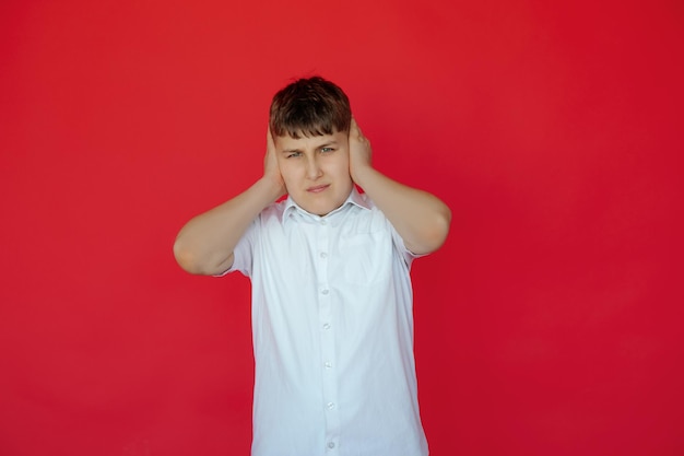 Ein Teenager im Hemd mit unzufriedenem Gesichtsausdruck will niemandem zuhören, der sich das Ohr zuhält