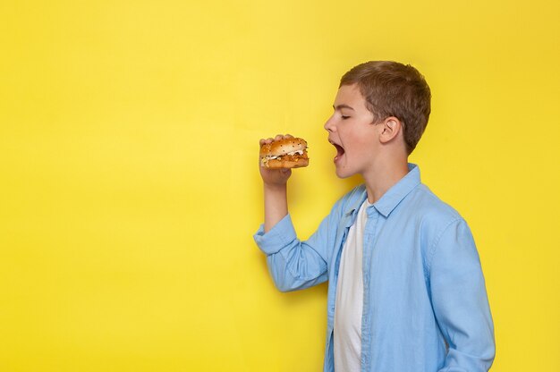 Ein Teenager in einem blauen Hemd beißt einen Burger