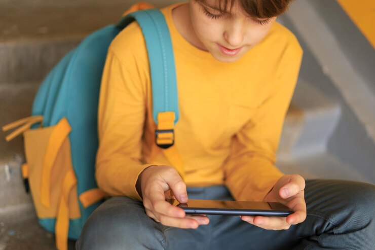 Ein Teenager in einem gelben T-Shirt spielt konzentriert online am Telefon und sitzt auf den Stufen