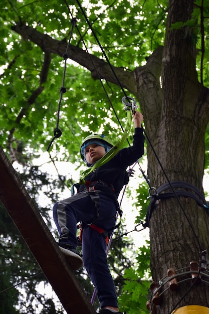 Ein Teenager in einem Schutzhelm klettert eine hängende Leiter in einem Seil-Freizeitpark