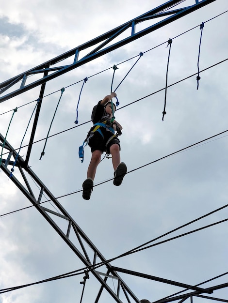 Ein Teenager in Sportausrüstung passiert vor bewölktem Hintergrund eine Hängebrücke