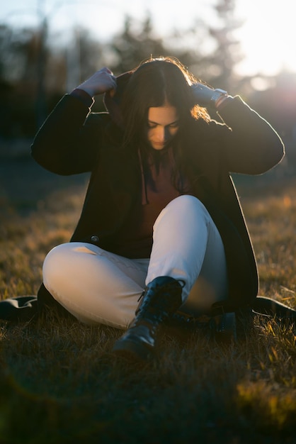 Ein Teenager sitzt alleine im Gras und zieht sich eine Kapuze an