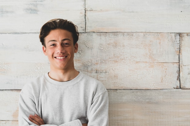 Ein Teenager zu Hause, der glücklich in die Kamera lächelt - einfaches Foto eines gutaussehenden jungen Mannes, der mit einer Holzwand im Hintergrund schaut