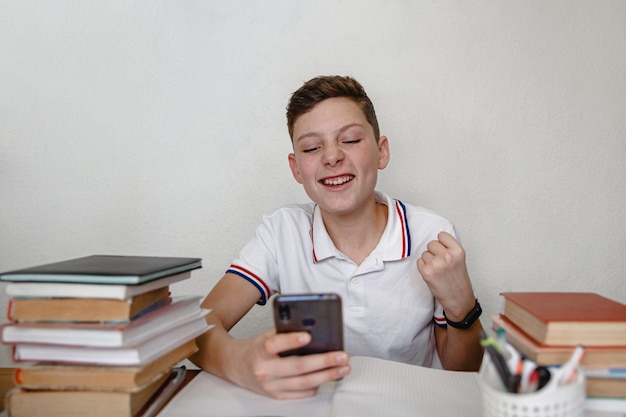 Ein Teenager zu Hause für Lehrbücher, die ein Smartphone betrachten, sieht die frohen Nachrichten